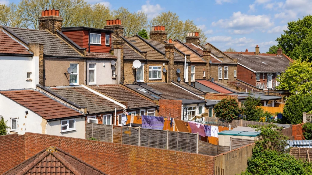 Rear elevations of neighbouring terraced houses in London, with extensions, fenced gardens, sheds and washing lines.