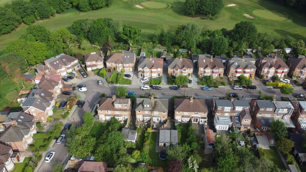 Aerial view of a suburban neighborhood with rows of semi-detached houses, neatly arranged gardens, and adjacent green golf course, showcasing residential planning and community layout.