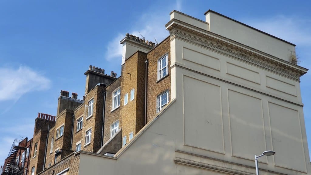 Unique perspective of the blank side wall of an end-terrace house contrasting against the detailed brickwork of adjacent terraced homes under a clear blue sky.