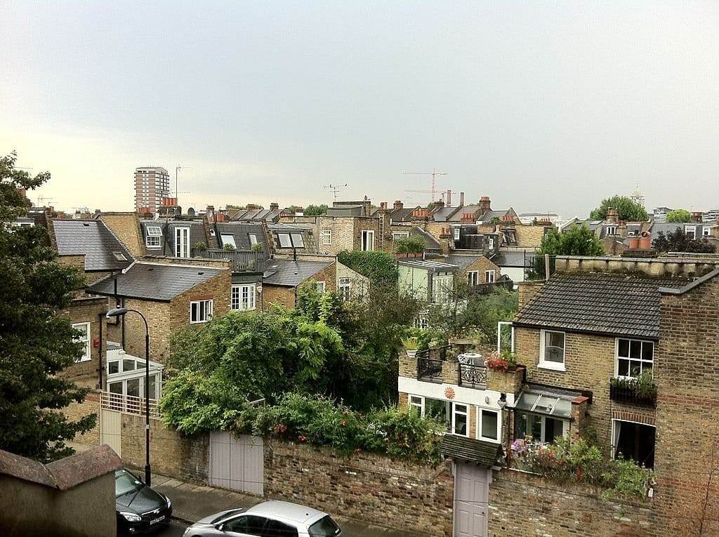 Overcast skyline view over a dense London neighborhood showcasing a mosaic of rooftops, dormer windows, and lush rooftop gardens with a backdrop of urban construction.