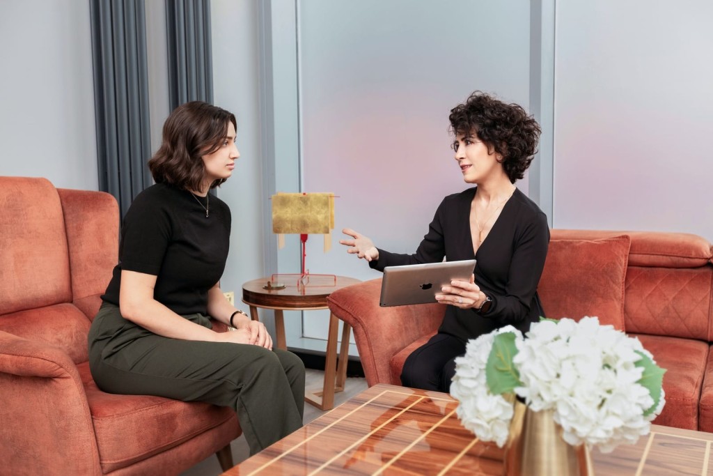 Professional consultation between a female planning consultant holding a tablet and a client in a modern office setting, discussing project details with elegant interior design in the background.