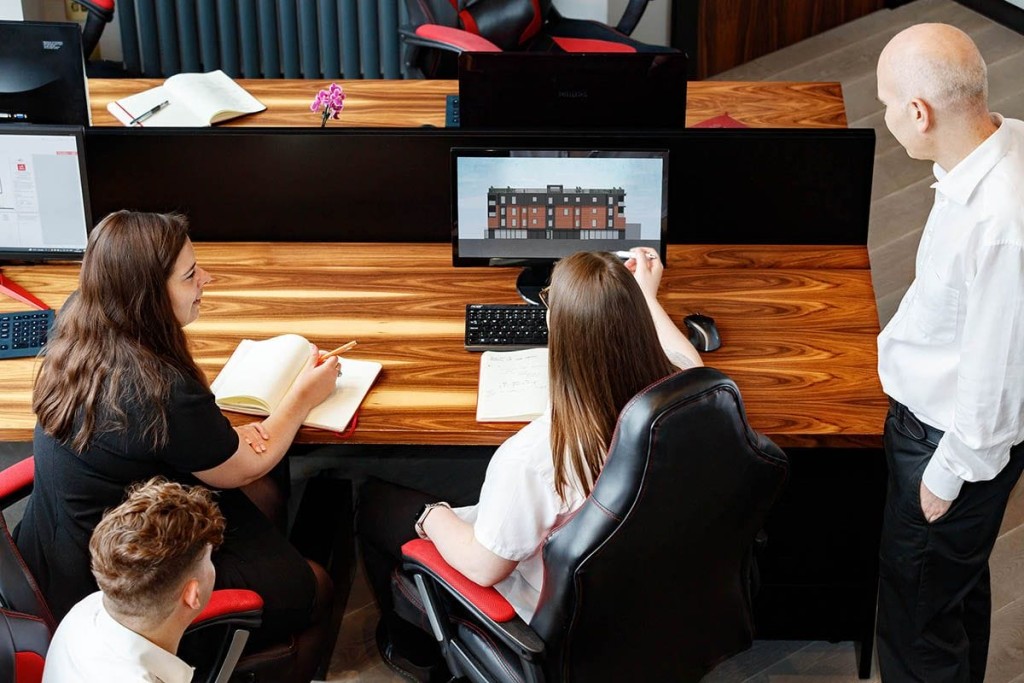 Team of architect and planning consultants collaborating on a computer design model at a wooden office desk, highlighting the detailed and team-oriented approach to planning and architectural design at Urbanist Architecture.