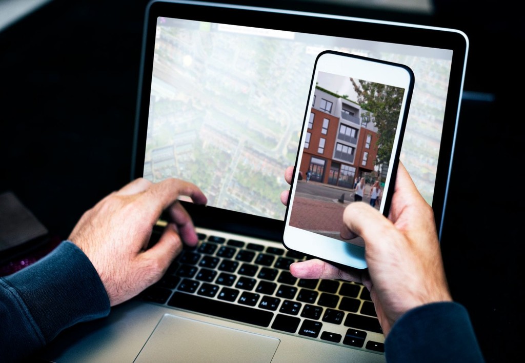 Architect's hands reviewing 3D architectural renderings of a new development project on a laptop and smartphone, illustrating the use of modern technology in feasibility studies and planning appraisals.