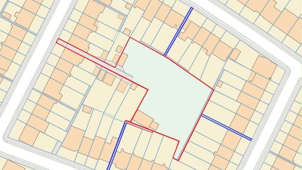 Urban land plot outlined in red for potential development, surrounded by a network of roads depicted in blue, amidst a grid of residential properties, indicating strategic planning in a suburban layout.