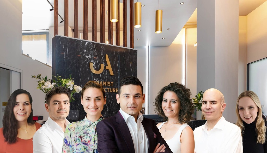 Professional team of architects and designers from Urbanist Architecture posing in their modern office, featuring a sleek marble reception desk with gold accents, elegant wood paneling, and stylish pendant lighting, representing a successful, creative workspace.