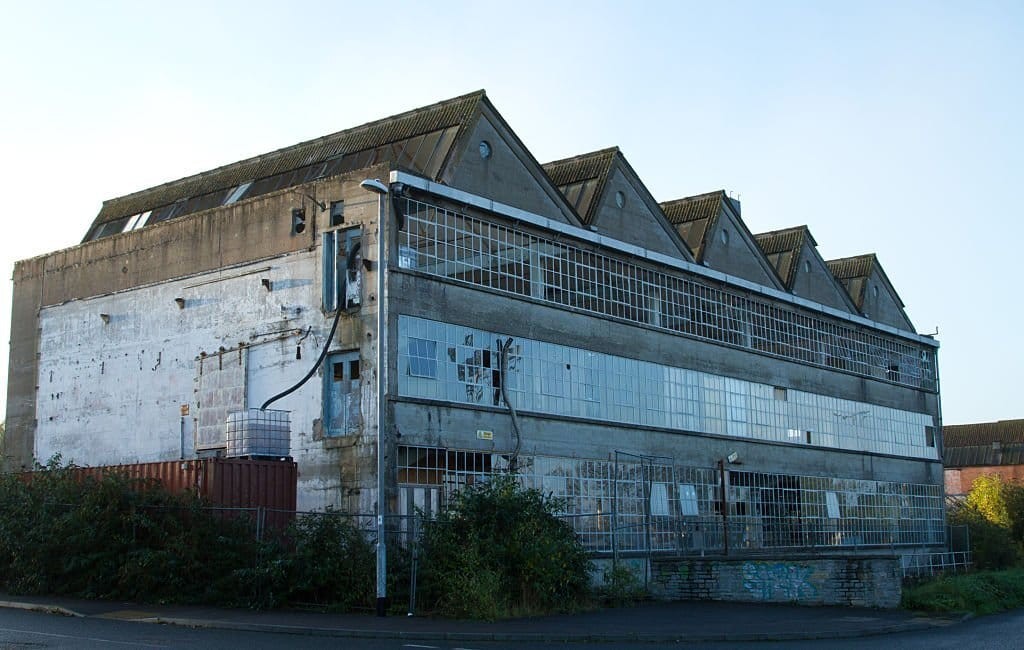 Abandoned industrial building with a dilapidated facade, broken windows, and overgrown vegetation, showcasing urban decay and industrial decline.