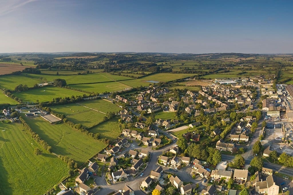 Wide aerial shot of a serene British village with residential homes and green fields, indicative of a typical rural settlement in the UK countryside, during golden hour.