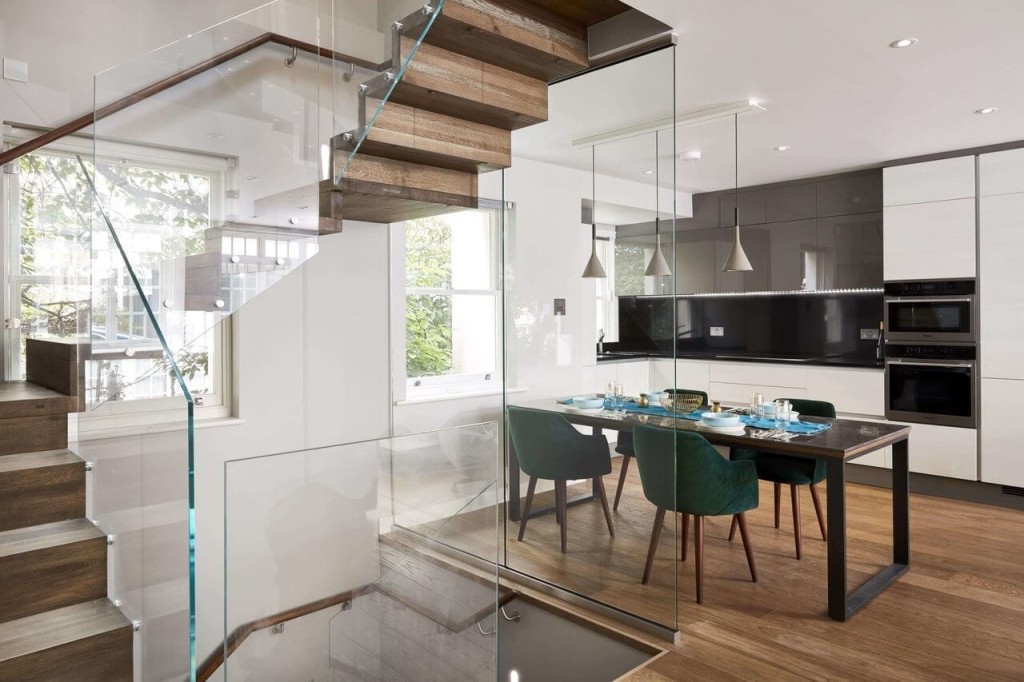 Interior design featuring a sleek kitchen with integrated appliances, a dining area with elegant green chairs, and a stylish wooden staircase with glass railings.