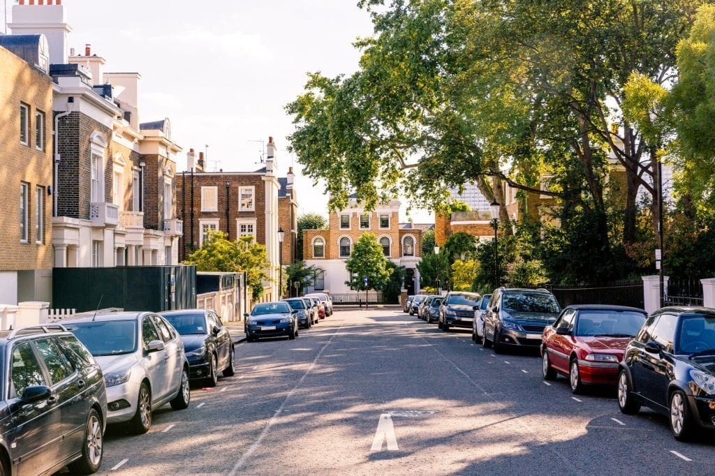 Charming London street lined with elegant townhouses and parked cars on a sunny day. Features classic Georgian and Victorian architectural styles, lush greenery, and a tranquil residential atmosphere. Ideal setting for top London interior designers to showcase their skills in transforming beautiful homes.