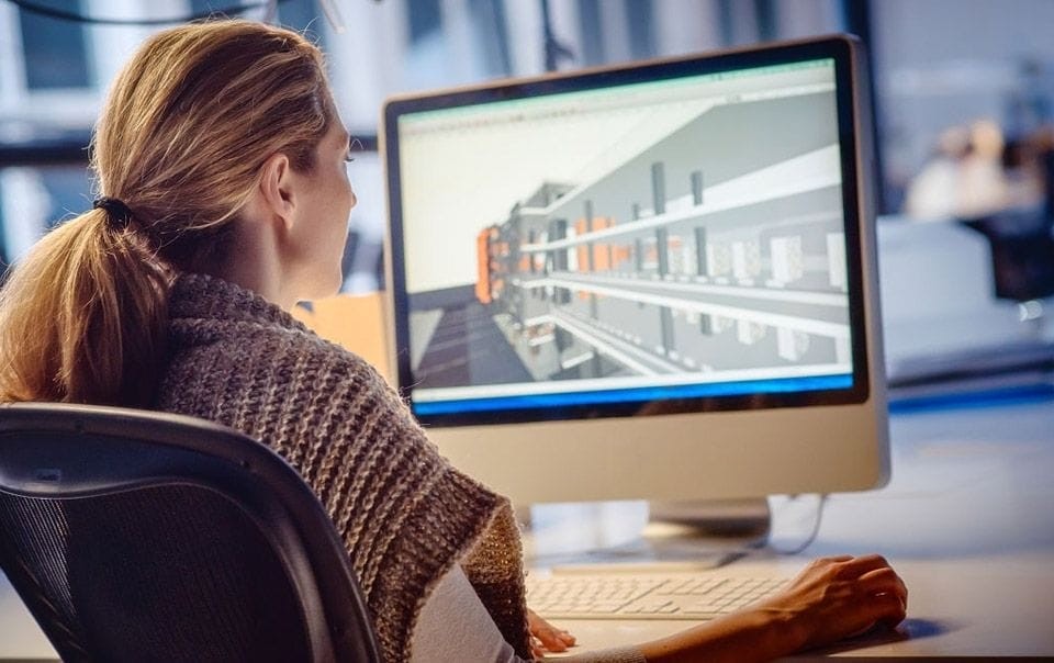 Architect sitting at her desk with her hair tied in a ponytail using BIM software for a large flatted development on her large screen desktop