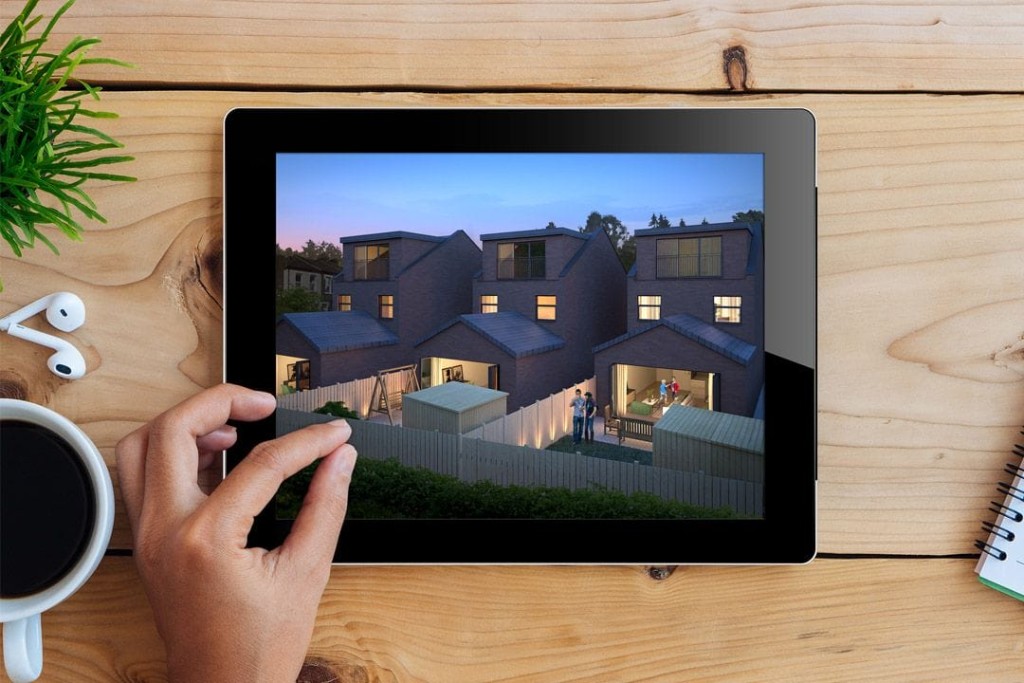 Left hand of a client pinching the screen to a black iPad laying on a wooden table with a mug of black coffee and white earphones about to zoom in on the virtual renders for the development of three identical triple storey houses with a rear dormer and spacious back gardens with some solar powered garden lights