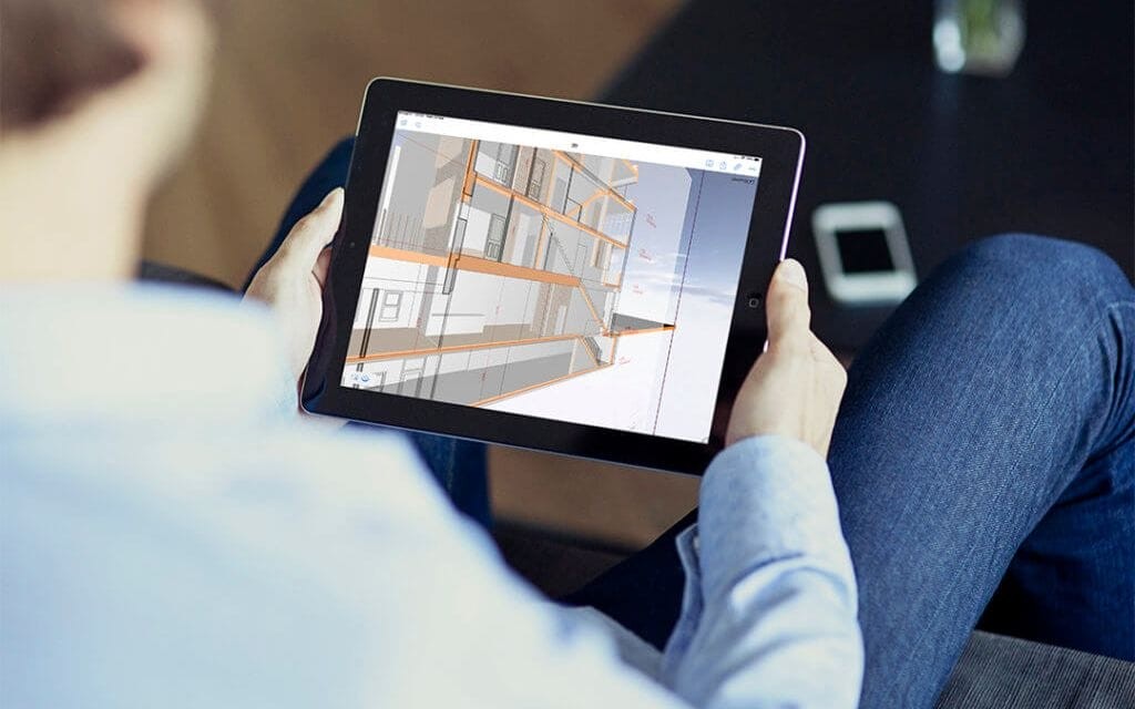 Client in a pale blue shirt and jeans sitting on a comfortable chair whilst holding a black iPad to review the BIM model for his latest flat development project in central London