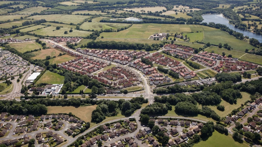 Aerial view of a residential development set within open countryside, showing nearby roads, fields, woodland and a lake.