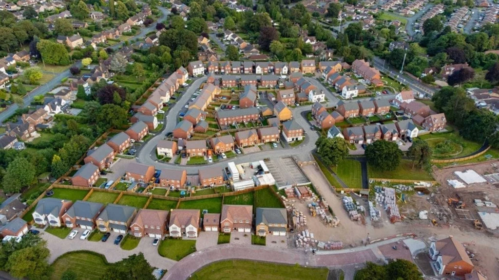 Aerial view of a residential housing development with surrounding gardens, roads, trees and an active construction area.