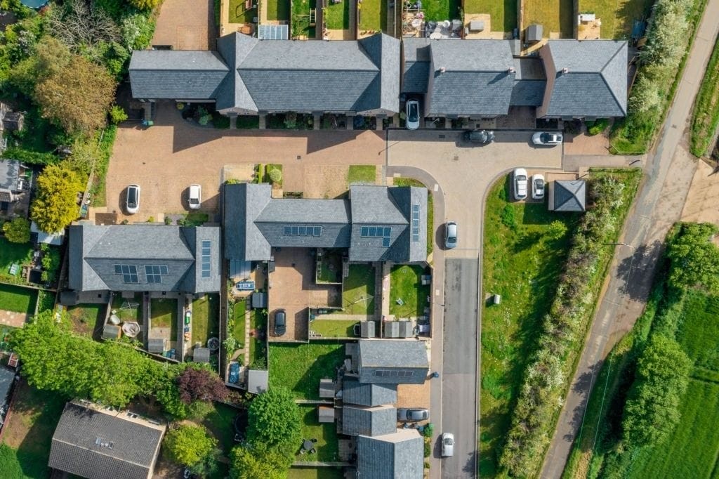 Aerial view of a luxury housing estate with interconnected slate-roofed houses, landscaped gardens, and a winding driveway, showcasing upscale residential architecture and suburban planning.