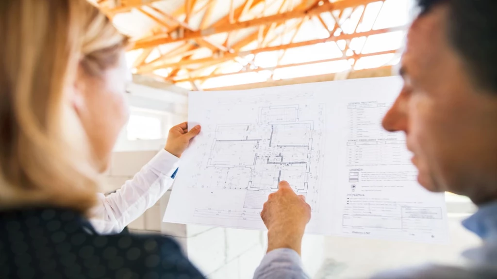 Architects reviewing detailed building plans on a construction site, exploring international models for better housing and infrastructure delivery.