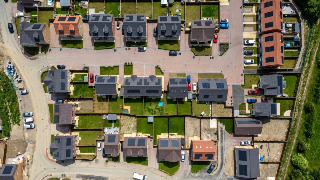Aerial view of a newly completed housing development in the UK, showing homes with rooftop solar panels, private gardens, driveways and internal access roads.