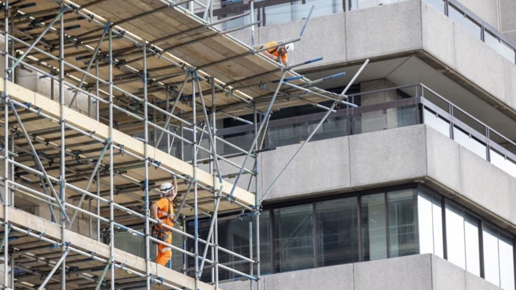 Construction worker stacking bricks on a scaffolding at a building site, representing the high labour costs and shortage of skilled workers in the UK construction industry. The image highlights one of the key reasons for the expensive yet subpar housing quality in 2024, as discussed in the article about housing costs and construction challenges in the UK.