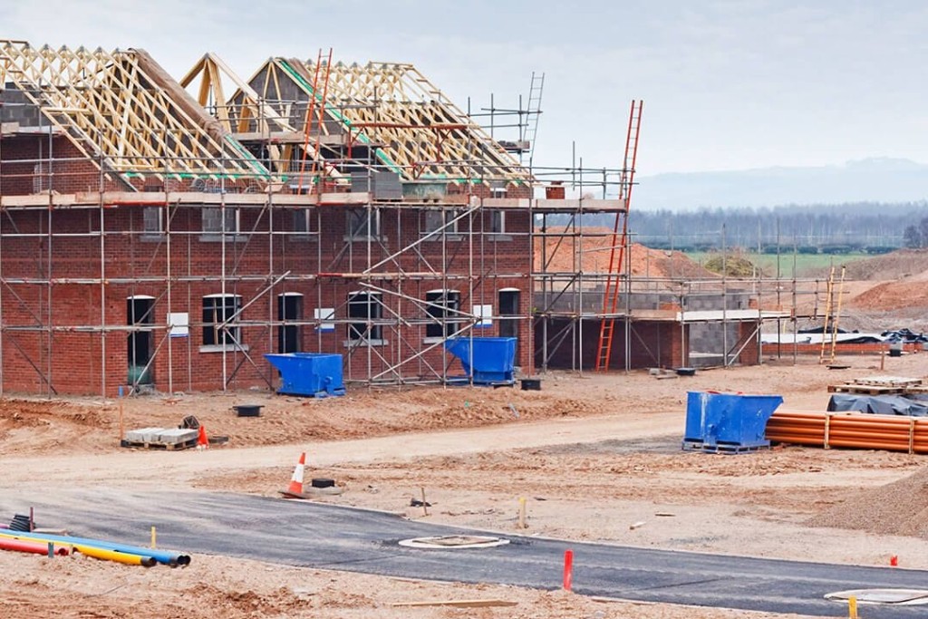 Residential construction site featuring partially built brick houses with scaffolding and roof trusses in place. The image illustrates the mid-construction phase of new housing development, highlighting the structural framework and ongoing building processes necessary for compliance with building regulations and standards.