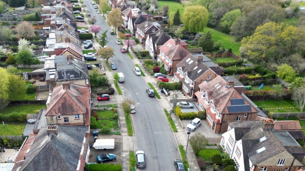 Aerial streetscape view of a residential street of large semi-detached houses with quite a few approved and developed dormer extensions, solar panels installations and rear extensions