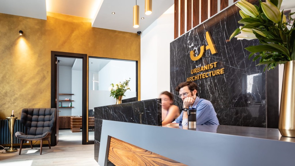 Luxurious architectural firm reception area with a marble desk featuring the Urbanist Architecture logo, elegant gold accents, and modern furniture, with staff busy at work.