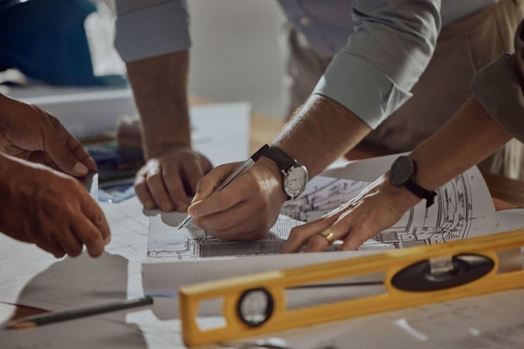 Close-up of hands of architects working on a blueprint with a ruler and a level, highlighting collaboration and precision in architectural planning.