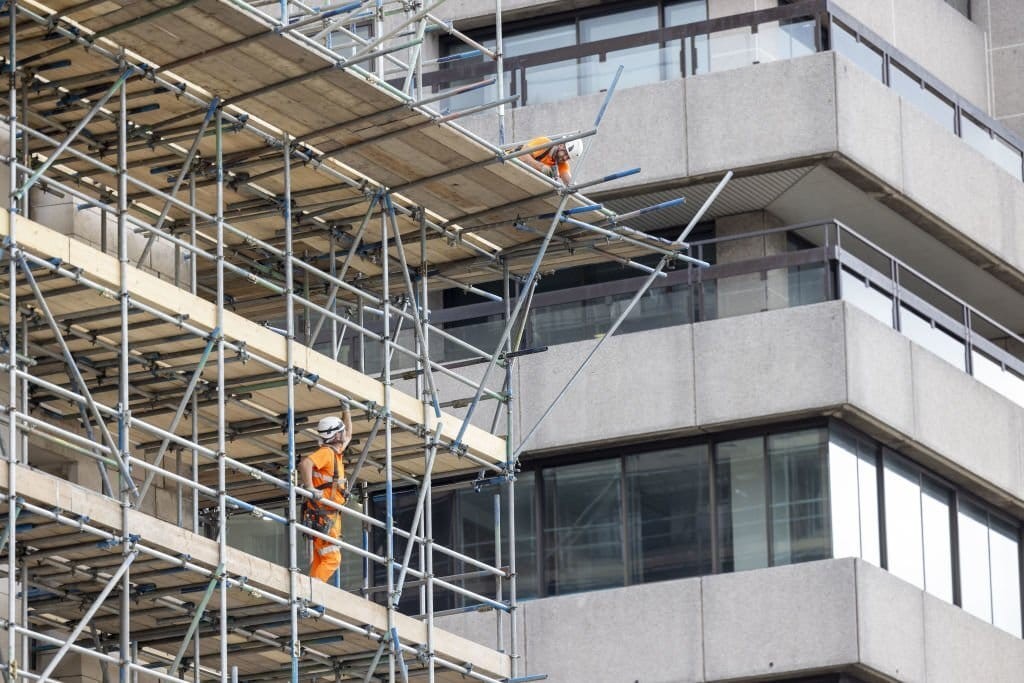 Construction workers in high visibility safety gear working on the scaffolding of a modern building facade, emphasising safety and development in urban construction.