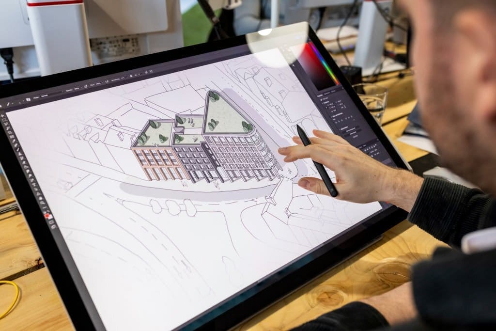 Architect using a digital pen on a graphic tablet to detail a 3D architectural rendering of a building complex, emphasising modern design technology in architecture.