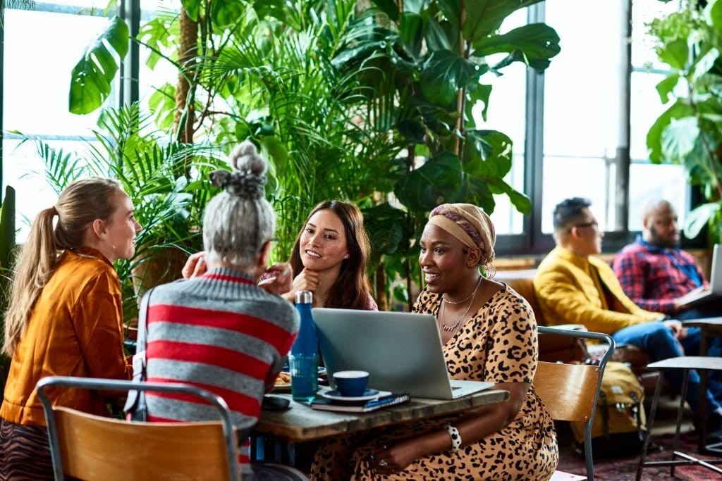 Diverse group of individuals engaging in a meeting at a co-working space with lush indoor plants, exemplifying collaborative work environment and creative interaction.