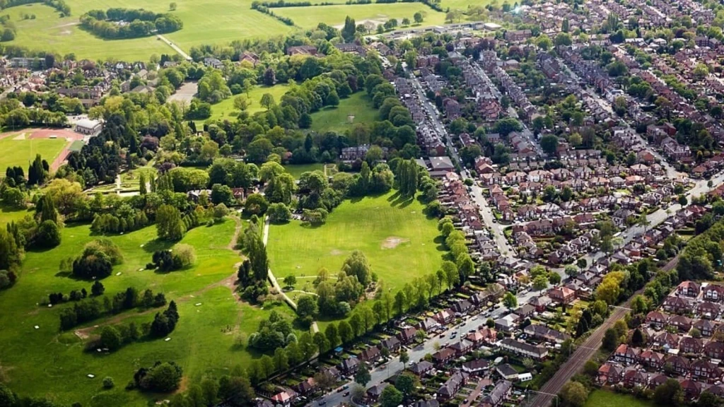 Aerial view showing dense suburban housing adjacent to large open green spaces, highlighting the tension between housing need and land availability within the planning system, as addressed through town planning and the National Planning Policy Framework.