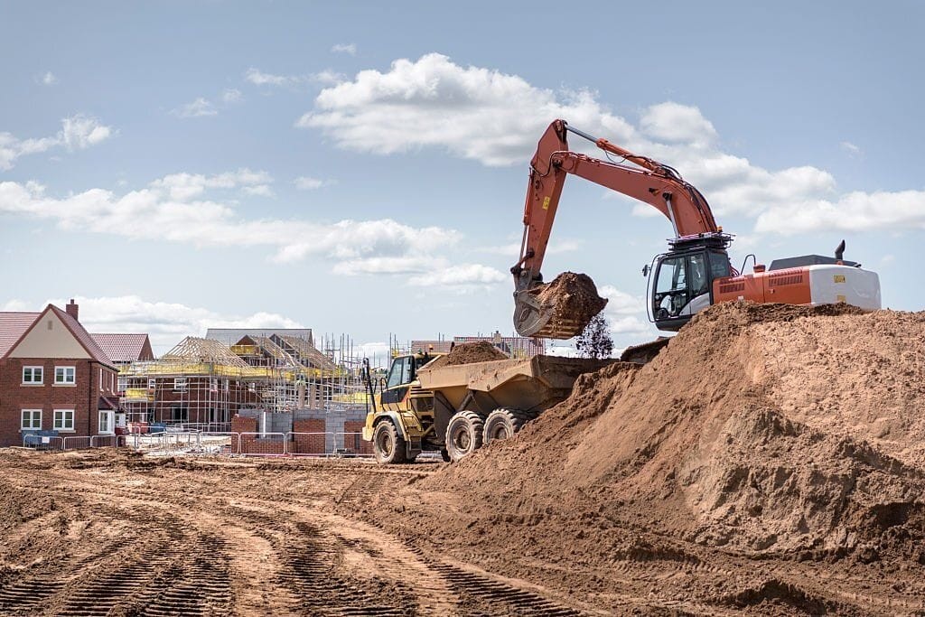 Construction site with heavy machinery excavating land, highlighting the redevelopment process of transforming disused petrol stations into residential housing. New homes are visible in the background, showcasing the potential for urban regeneration and efficient land use.