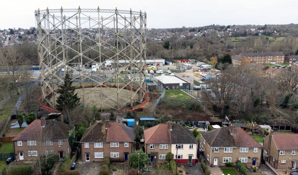 Aerial view of a residential neighborhood adjacent to a large, disused gas storage facility. This image highlights the potential for redeveloping underutilised industrial sites into housing, illustrating the opportunity for urban regeneration and efficient land use in densely populated areas. Ideal for discussions on brownfield development and sustainable urban planning.
