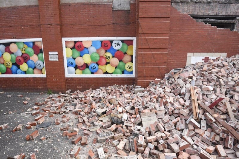 Piles of red bricks on the side of the currently demolished bingo hall with the remaining bingo number posters on the side of the property