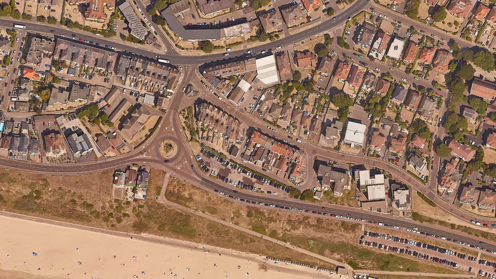 Aerial view of Southbourne Crossroads car park in Bournemouth, surrounded by residential buildings and near a sandy beach. The image highlights the potential for redevelopment of underutilised urban spaces into residential units, emphasising sustainable urban planning and community enhancement.