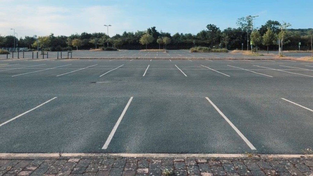 Empty car park with marked parking spaces in a prime urban location, surrounded by greenery, showcasing potential for redevelopment into residential flats. Ideal site for urban housing projects and sustainable development.