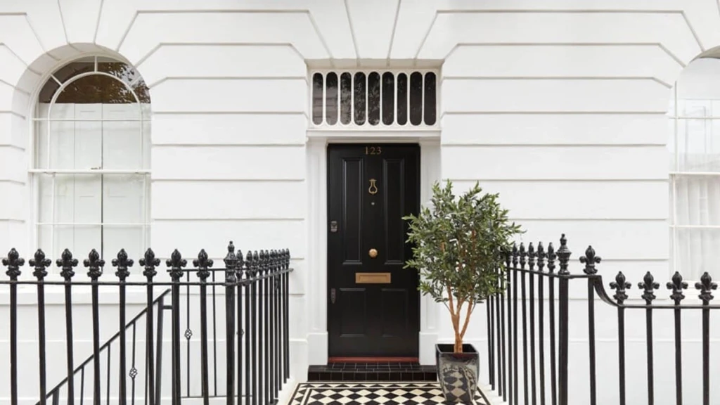 Front entrance of a classic Georgian townhouse in London, featuring a black door with brass hardware, white rendered façade, arched sash windows, and black-and-white tiled path. The image illustrates a property undergoing a deconversion development from flats back into a single-family home.