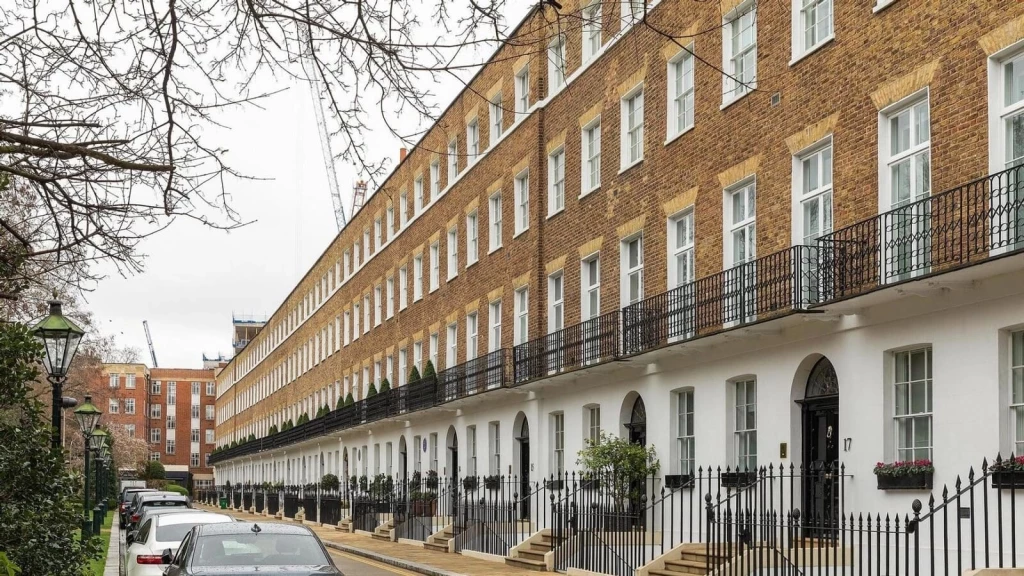 A row of elegant Georgian-style terraced buildings in Central London, featuring uniform brick façades, black wrought iron balconies, and white-painted lower storeys. Some properties appear to be amalgamated into larger flats.