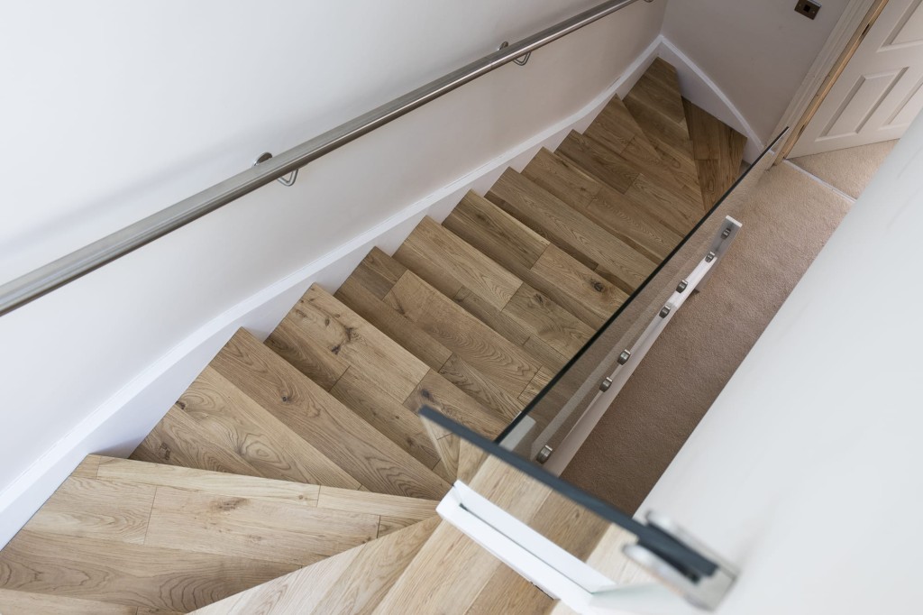 Modern wooden staircase and stainless steel handrail leading down to a carpeted floor, showcasing contemporary interior design and architecture.