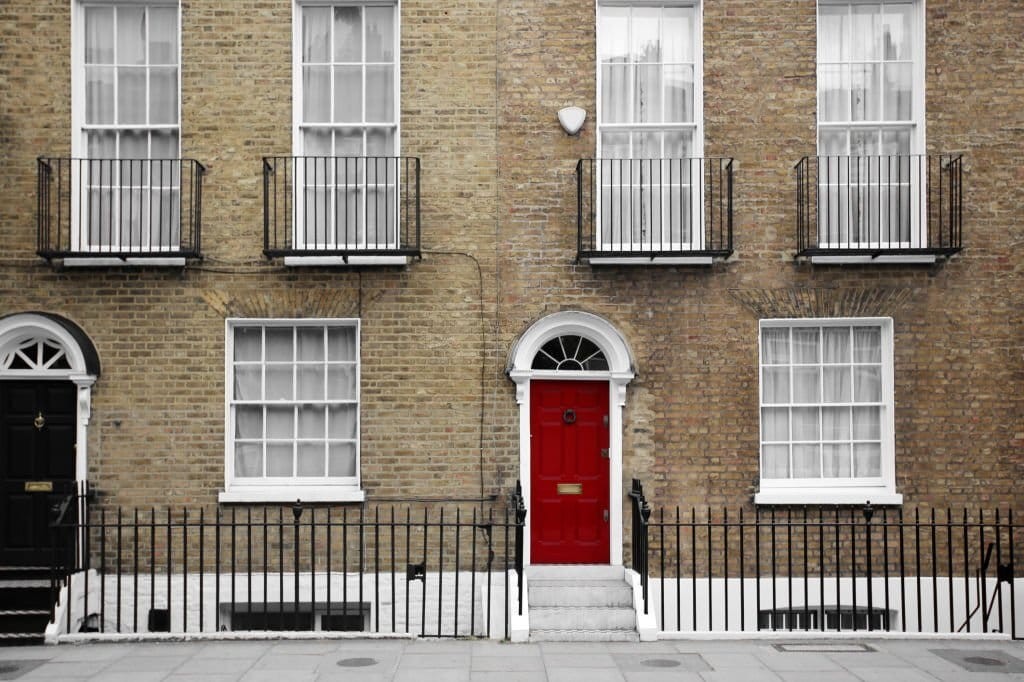 Traditional London townhouse with a distinctive red front door, symmetrical white-framed windows, and black iron railings on a classic brick facade.