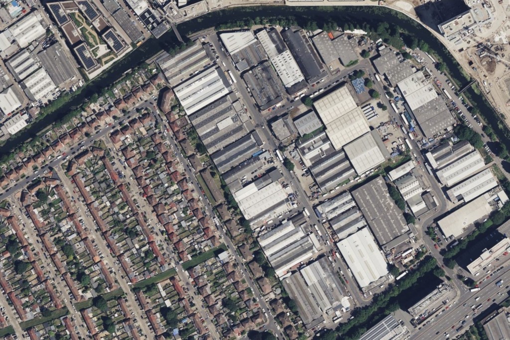 Aerial view of a neighbourhood outlined with dense greenery with the left hand side being residential with semi detached homes whilst on the right hand side is an industrial and commercial zone