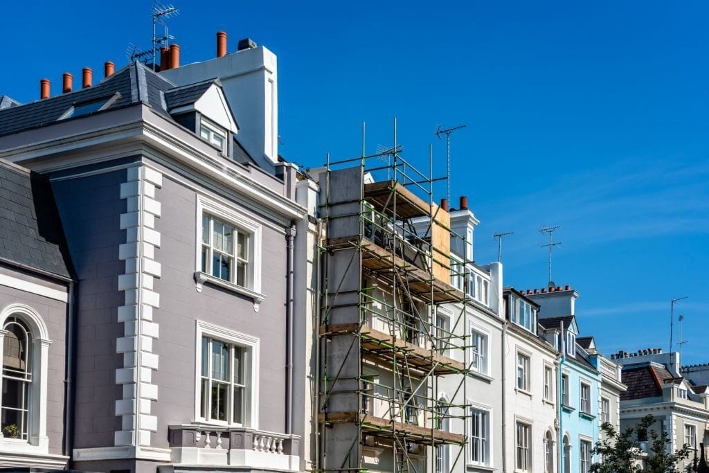 Elegant row of Victorian townhouses under renovation with scaffolding on the exterior, against a clear blue sky, reflecting urban development and restoration.
