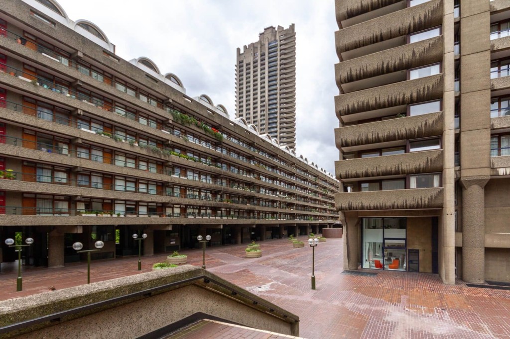 Exterior view of a large, concrete residential block with multiple storeys of apartments, showcasing Brutalist architecture. The image highlights the expansive courtyard, surrounding tall buildings, and distinctive balcony designs.