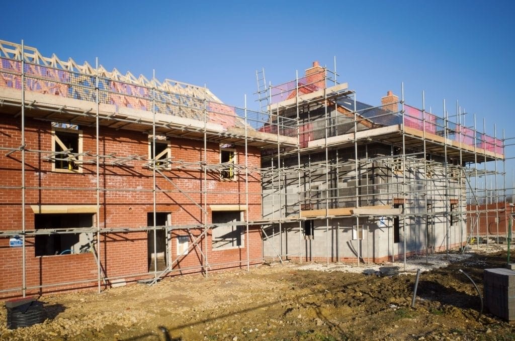 Construction site of a residential building with scaffolding and brickwork in progress, illustrating the development phase of new homes under clear blue skies.