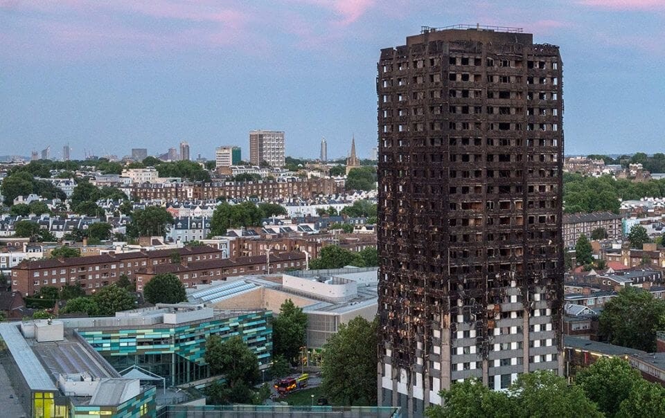 Remains of the burned-down Grenfell tower high-rise residential building against London city backdrop, highlighting the aftermath of a devastating urban fire and the importance of fire safety in architectural design.