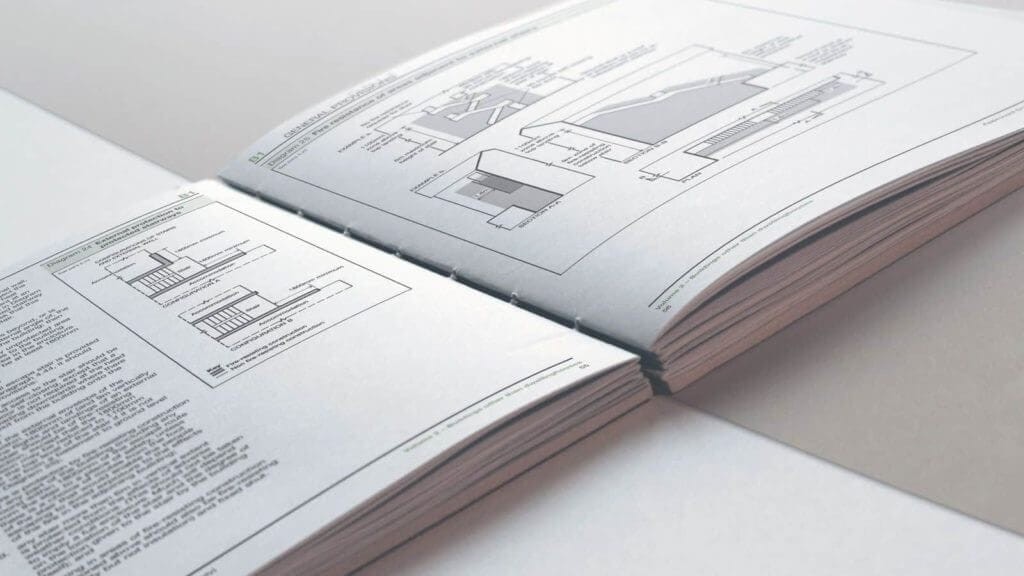 Open technical guidebook displaying detailed architectural drawings and building specifications, on a white surface with focused lighting, emphasising precision in construction planning.