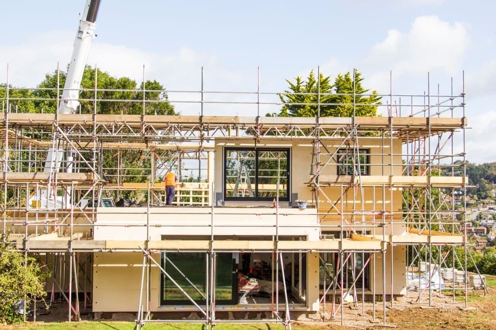 Construction site with workers and scaffolding around a new build house, illustrating the development process in suburban housing with a backdrop of a scenic town.
