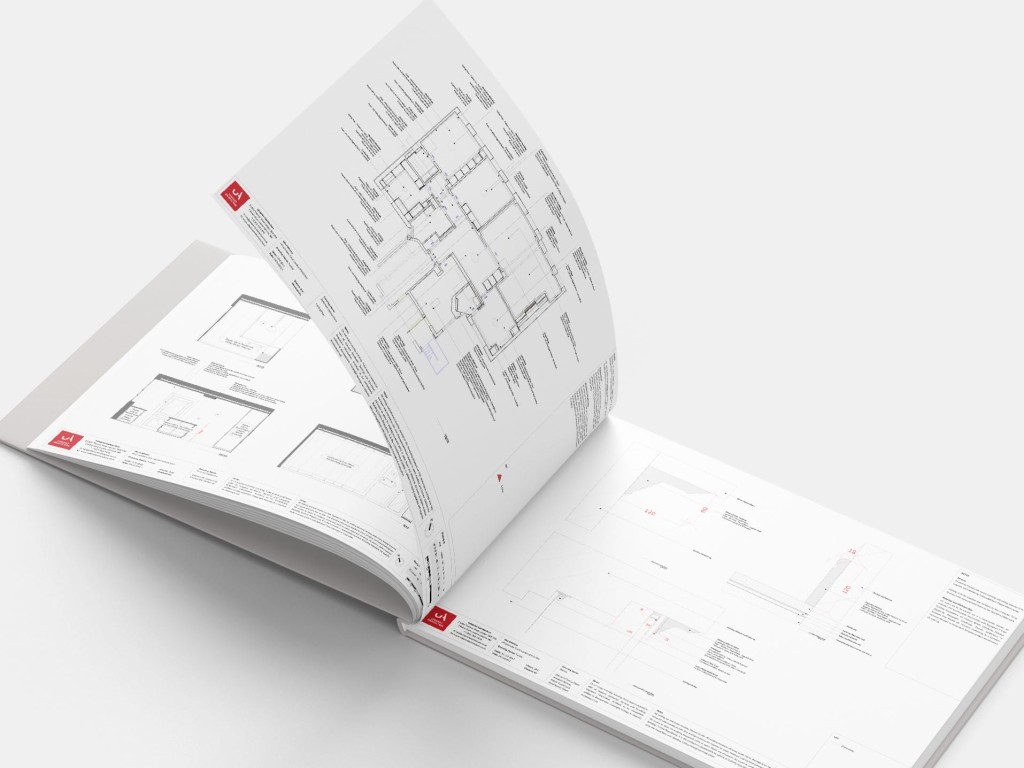Professional architectural plans printed in a design book, with detailed building sections and floor plans visible, showcasing the technical aspect of architectural design and planning.