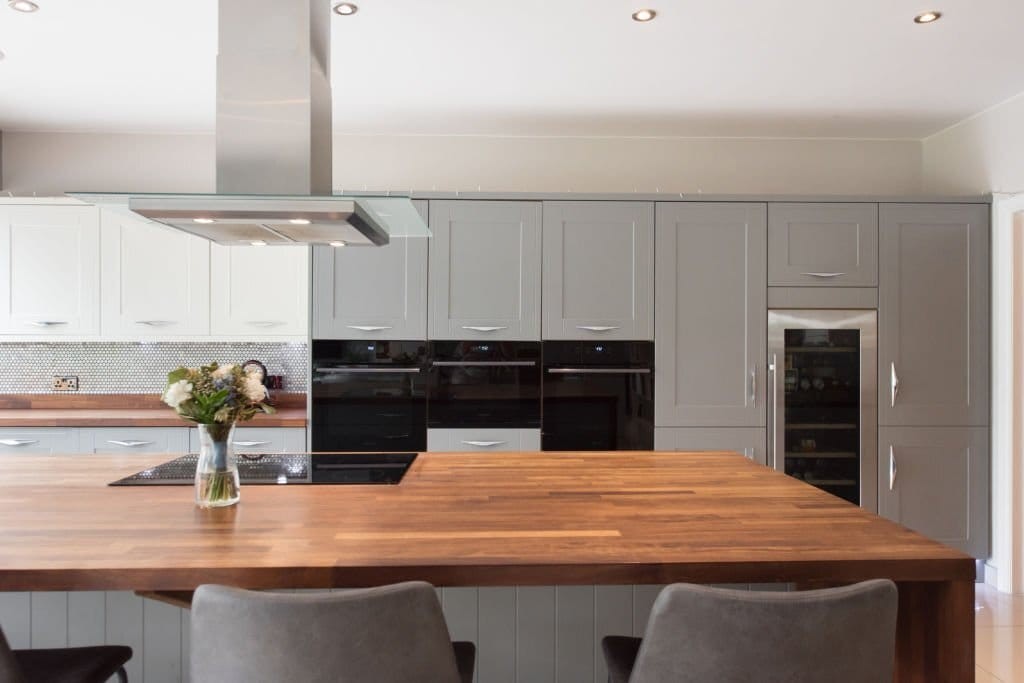 Modern kitchen interior with grey cabinetry, integrated appliances, and a large wooden island, highlighted by natural light and complemented by a vase of fresh flowers for a homely touch.