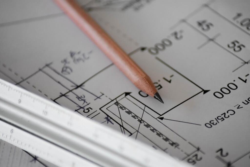 Sharpened natural wood pencil and metail ruler lay on top of architectural detail drawings