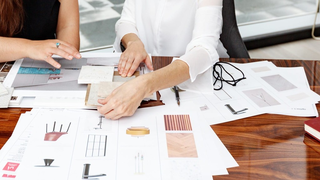 Interior designers examining material samples and architectural drawings spread out on a wooden table for a project planning session.